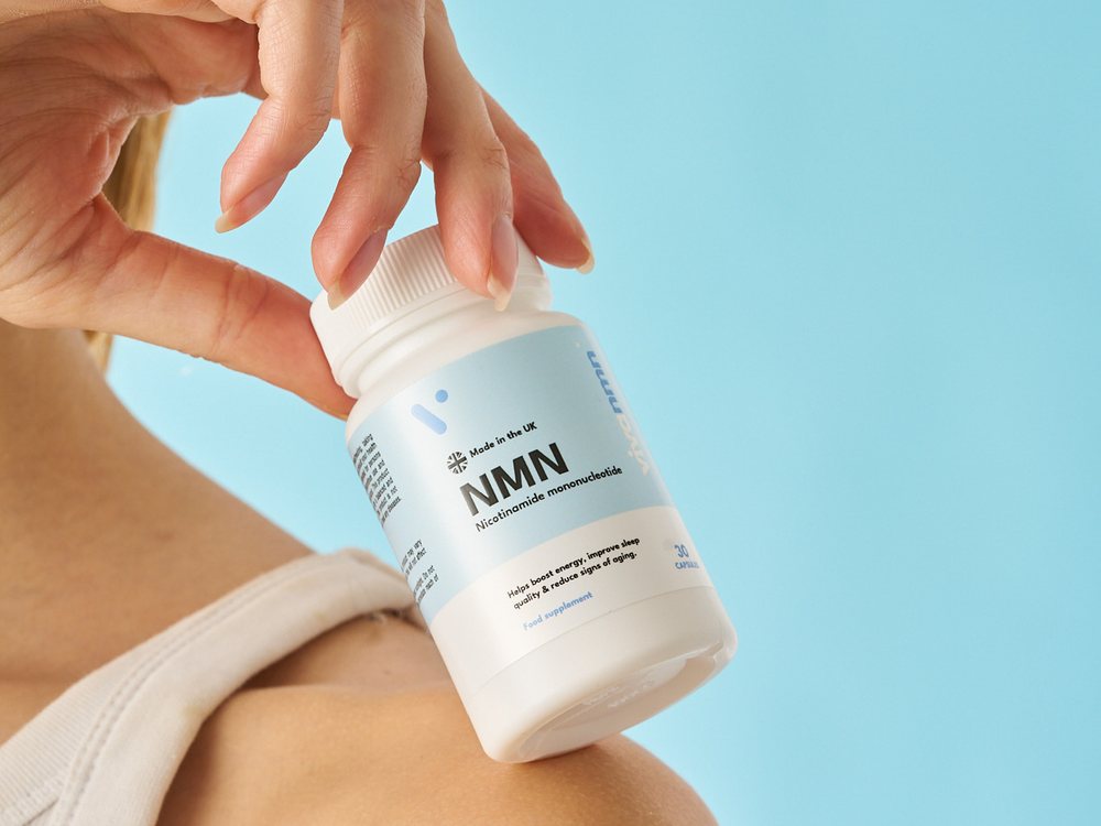 A bottle of vivanmn NMN held on a woman's shoulder against a blue background